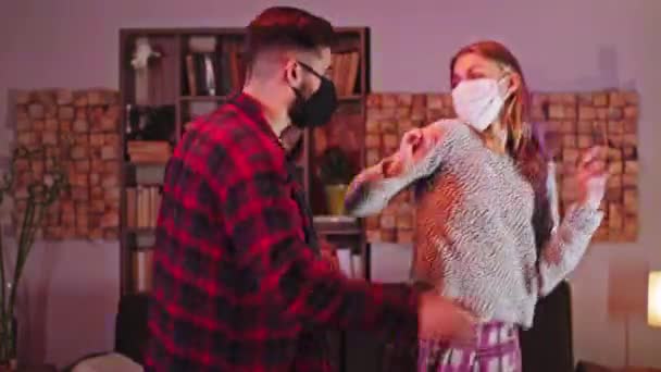 Happy moments for a beautiful couple in the quarantine at home dancing in the dark living room enjoying the time together they wearing protective mask Covid-19 — Stock Video