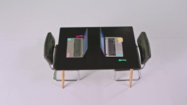 Beyaz bir arka planda, siyah bir ofis masasının videosunu çekiyor. İki dizüstü bilgisayar ve birkaç küçük renkli kağıt.