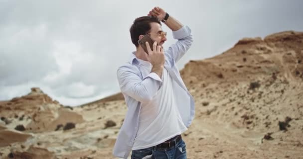 Jóképű fickó napszemüvegben beszél telefonon, és élvezi az időt a csodálatos táj — Stock videók