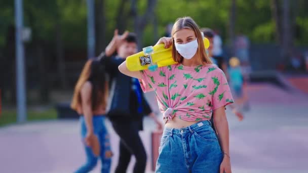 Bella giovane donna in uno skate park urbano davanti alla telecamera togliti la maschera protettiva in pandemia prendi un po 'd'aria fresca prima di iniziare un giro con lo skateboard coronavirus 2019. 4k — Video Stock