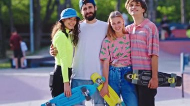 Kaykay parkı mutlu ve gülümseyen bir grup erkek ve kadın kameranın önünde kaykaylarını tutarken poz veriyorlar.