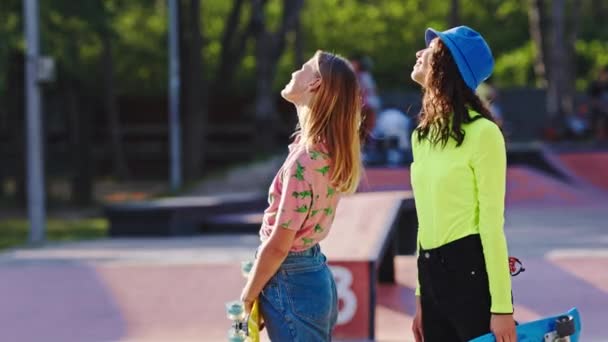 W słoneczny dzień w środku skate parku dwie dobre przyjaciółki cieszące się czasem spędzonym razem uśmiechają się i rozmawiają przed rozpoczęciem przejażdżki. 4k — Wideo stockowe