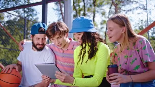 Jovens grupo de amigos multiétnicos mulheres e homens aproveitam o tempo juntos usando um tablet eletrônico assistindo algum filme no parque moderno — Vídeo de Stock