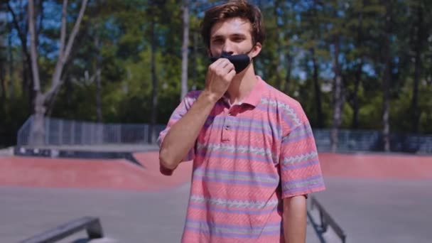 Отличный молодой человек в городском скейт-парке в черной защитной маске, чтобы защитить вирус Ковид-19 перед камерой — стоковое видео