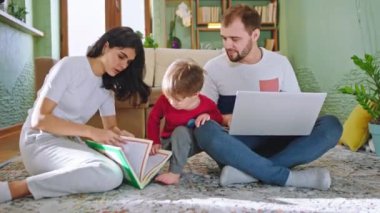 Geniş oturma odasında mutlu bir aile yerde oturmuş çocuklarla kitap okuyor ve evde iyi vakit geçiriyorlar.