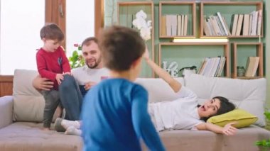 Mutlu ve gülümseyen büyük bir aile kanepeye oturup çocuklarıyla komik oyunlar oynarken heyecanlı hissediyorlar ve aileleriyle anın tadını çıkarıyorlar.