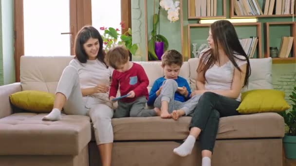 彼らはソファの上に家に座っている間、彼らの子供たちと一緒に遊んで幸せな笑顔の母親ゲームをプレイするためにスマートフォンを使用して子供たちは自宅で安全に滞在隔離時間で新しいコロナウイルス2019 — ストック動画
