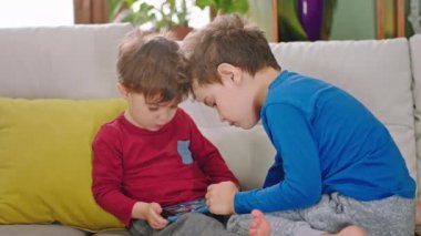Komik iki küçük kardeş oturma odasındaki kanepede birlikte oynadıkları akıllı telefonu kullanarak çok güzel vakit geçiriyorlar. ARRI Alexa Mini 'de çekilen