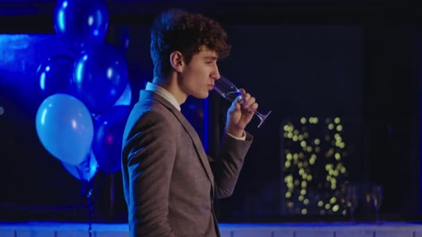 Na večírku charismatický mladík pije šampaňské ze sklenice a cítí se tak uvolněně, že nosí neformální oblek — Stock video