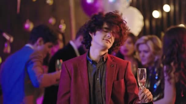 Very charismatic guy with curly hair in front of the camera dancing moving funny enjoying the evening at big glamorous party he holding a glass of champagne. 4k — Stock Video