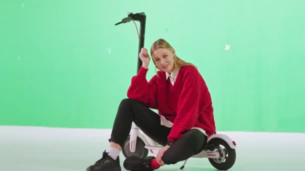 Posa di fronte alla fotocamera carismatica capelli biondi giovane donna mentre si siede su un moderno concetto di scooter di uno studio chiave croma — Video Stock