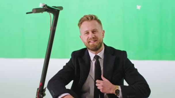 Modern green studio businessman in a black suit take a sit on his modern electric scooter and posing in front of the camera. 4k — Stock Video