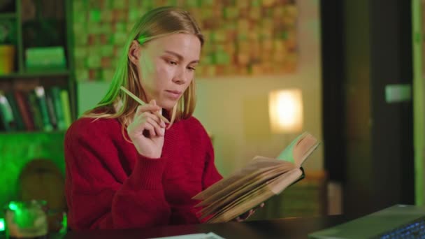 Mujer guapa leyendo un libro en la biblioteca para estudiar algo para su proyecto universitario frente a la cámara — Vídeos de Stock