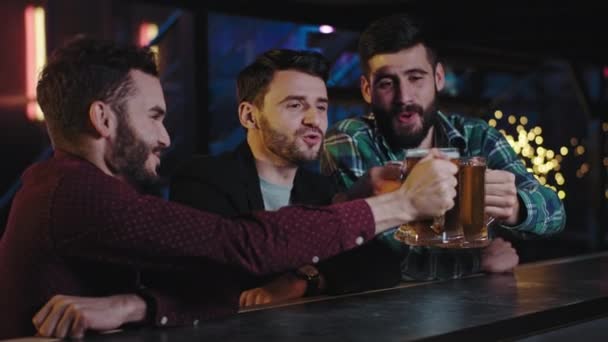 Група друзів харизматичні хлопці в пабі, сидячи за барним столом, починають пити великі келихи свіжого пива, вони підбадьорюють окуляри і відчувають себе так розслабленими — стокове відео