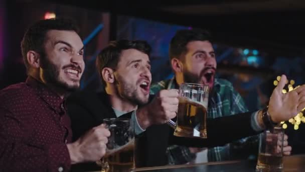 Świetnie wyglądający faceci bardzo emocjonujący oglądając mecz w telewizji w barze sportowym świętują zwycięstwo wiwatując szklankami piwa są bardzo podekscytowani. Zdjęcia z kamery filmowej ARRI — Wideo stockowe