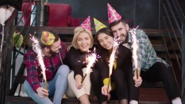 Modern bir ofis stüdyosunda merdivenlerde güzel görünümlü, etnik çeşitlilikte genç insanlar ellerinde ışıltılarla kameraya bakarlar.