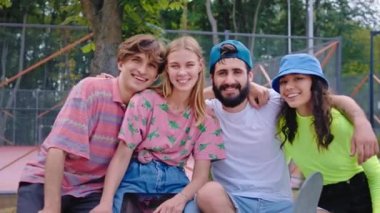 Modern kaykay parkı portresi. Çok ırklı güzel bir arkadaş grubu. Şık kıyafetler ve büyük bir gülümsemeyle kameraya bakıyor.