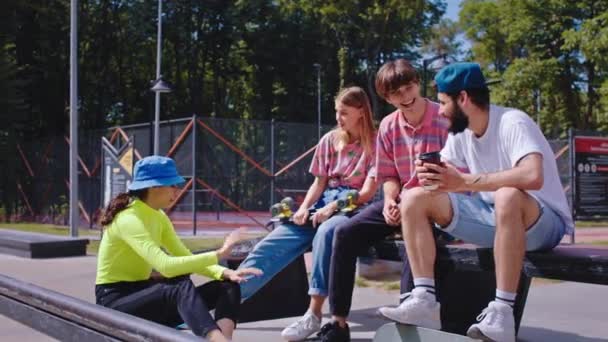 Снаружи в городском скейт-парке классная группа хипстерских друзей проводят время, общаясь перед поездкой на скейтборде, они улыбаются и чувствуют себя счастливыми. — стоковое видео