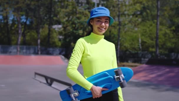 Усміхнена красива азіатка в міському скейтборді вона тримає свій скейтборд і дивиться прямо на камеру має гарний настрій, перш ніж почати їзду зі скейтбордом. 4k — стокове відео
