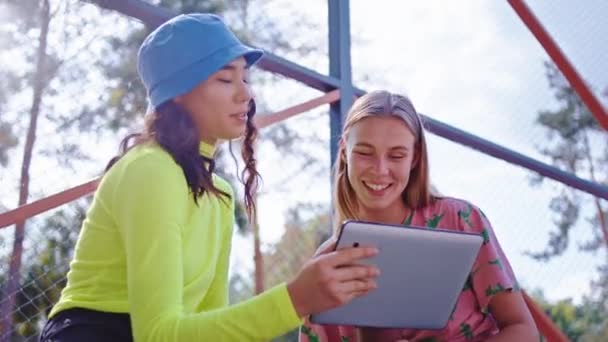Schöne Damen mit einem breiten Lächeln genießen die Zeit draußen im Park, sie benutzen ein elektronisches Tablet, um etwas zu sehen — Stockvideo