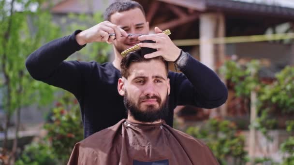 Hombre de gran aspecto con una gran sonrisa tienen una discusión con el peluquero mientras que hacer un corte de pelo en casa en el medio del jardín — Vídeos de Stock