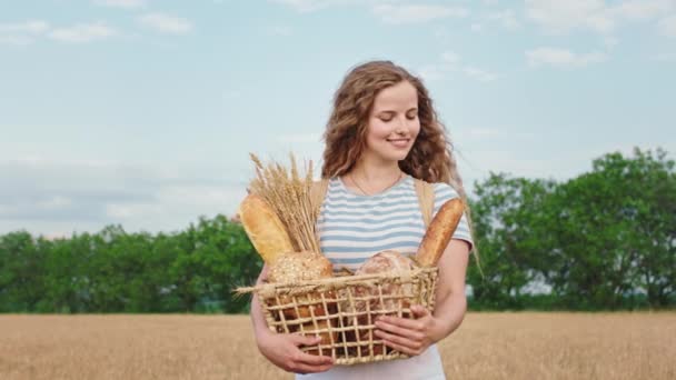 Giovane donna felice e sorridente davanti alla telecamera guardando dritto tiene una scatola piena di pane fresco e annusa il pane guardando la macchina fotografica. 4k — Video Stock