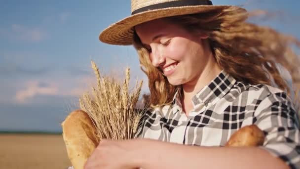 Nahaufnahme einer jungen, gut aussehenden Bäuerin mit Hut, die inmitten eines großen goldenen Weizenfeldes eine Kiste voller Brot hält. Schuss auf ARRI Alexa Mini — Stockvideo