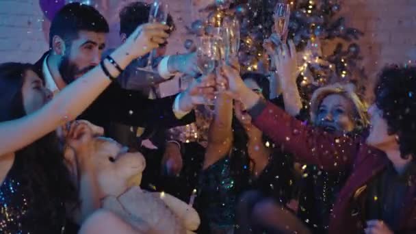 Junto al grupo de amigos del árbol de navidad celebrando juntos patanes de confeti por todas partes, les aplauden con copas de champán. — Vídeo de stock