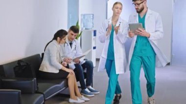 Modern hastane koridorunda çok ırklı kadın ve erkek doktorlar hastanın gelecekteki tedavisini tartışıyor. Resepsiyonda durup dijital tablete bakıyorlar.