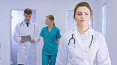 Kameranın önünde modern bir hastane koridorunda yetişkin bir kadın doktor kameranın arka planında yürüyordu. Meslektaşları, başhekim ve genç hemşire bir konuşma yapıyorlardı.