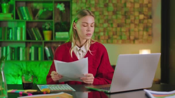 Estudiante concentrada rubia haciendo su proyecto de la universidad en casa usando la tableta electrónica que escribe algo en el papel y hacer cara de pensamiento — Vídeos de Stock