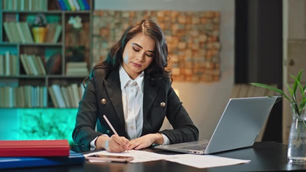 Mulher de negócios bonita concentrada que trabalha no seu lugar de escritório escreve alguns documentos e digita no computador portátil — Vídeo de Stock