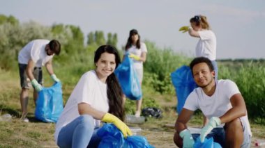 Kameranın önünde güzel bir bayan ve karizmatik bir Afro-Amerikalı adam plajda mavi plastik torbalarla oturuyor ve diğer gönüllülerle çöp toplayarak eğleniyor. ARRI 'de çekilen