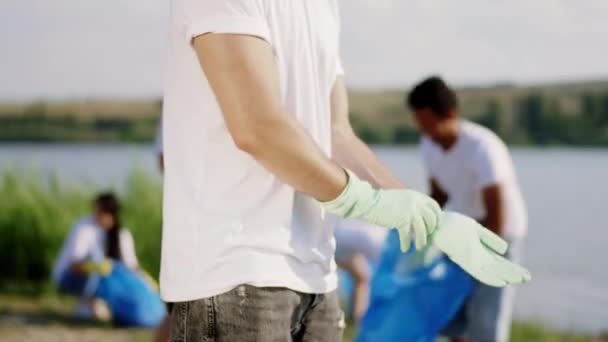 Vor der Kamera am Strand ziehen Freiwillige die Schutzhandschuhe an, bevor sie mit dem Aufräumen des Mülls beginnen — Stockvideo