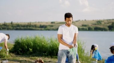 Çöpleri toplamaya başlamadan ve mavi plastik torbaları toplamaya başlamadan önce koruyucu eldiven takan Afro-Amerikalı gönüllü adama özen gösterme kavramı
