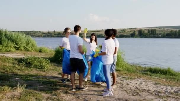 Grupo multirracial de jóvenes voluntarios terminan de limpiar la basura del lado de la playa y luego todos juntos al final aplaudiendo entre sí y dando un gran abrazo como un equipo fuerte. Disparo en ARRI — Vídeo de stock