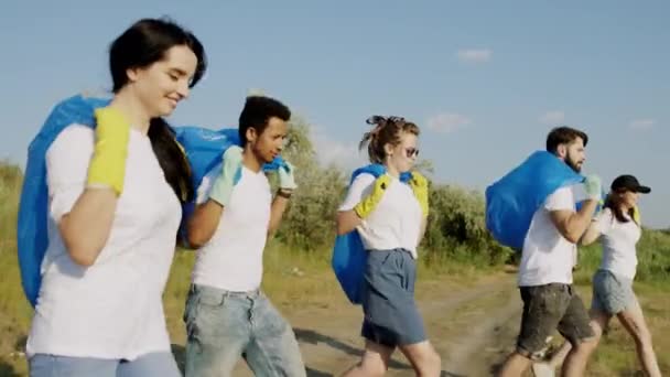 Des bénévoles multiraciaux devant la caméra qui courent ensemble tenant de gros sacs en plastique pour les ordures et commencent à ramasser les ordures de la plage. Tourné sur ARRI Alexa Mini — Video