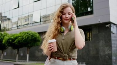 Sokakta uzun saçlı, akıllı telefonuyla konuşan ve elinde kahve bardağıyla uyanan hoş bir bayan.