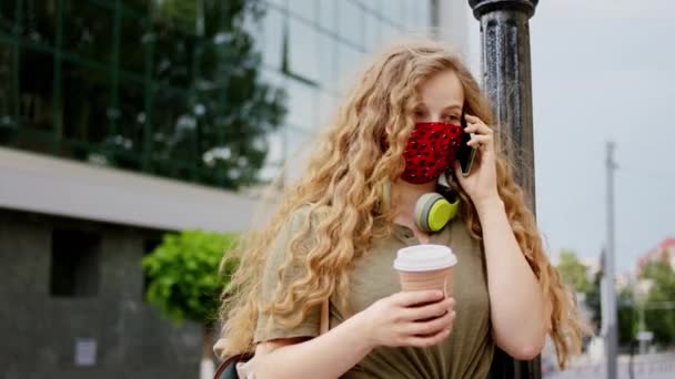 2019 년 코로나 바이러스 유행병에서 얼굴에 보호 마스크를 쓴 아름다운 여성이 커피 잔을 들고 휴대폰으로 말하는 모습 — 비디오