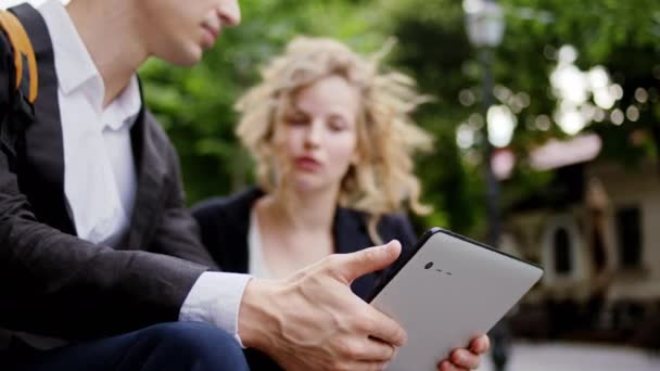 Gelukkig en glimlachend grote zakenman en zijn assistent mooie dame hebben een discussie samen terwijl kijken door middel van een digitale tablet in het midden van de straat — Stockvideo