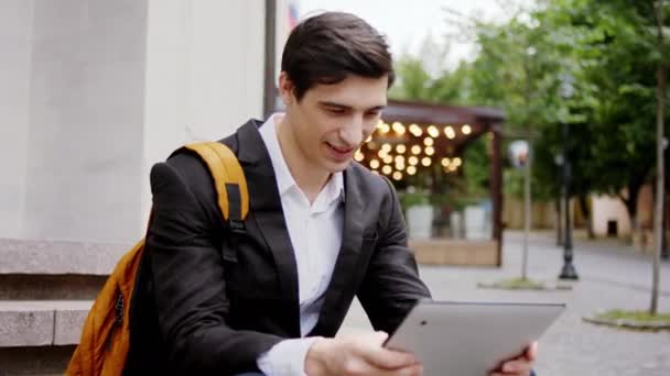 Guapo joven empresario tomar un asiento en las escaleras en el medio de la calle y se concentró trabajando en su tableta electrónica — Vídeo de stock