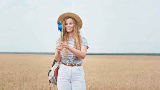 風のスピナーで遊んで小麦畑の真ん中のカメラの前で美しい田舎の女性 — ストック動画
