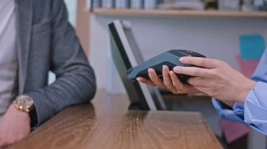 Kameraman bayana yakın çekim. Terminali müşteriye veriyor. Kredi kartıyla ödeme yapıyor.