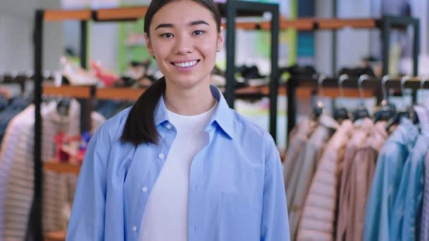 Asiatique jeune femme vendeur dans un magasin de vêtements regardant directement à la caméra portrait elle ont un grand sourire et dents blanches — Video