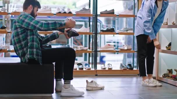 Przystojny klient usiądzie na kanapie w sklepie obuwniczym i zrobi różnicę między butami, które chce kupić. Strzał na ARRI Alexa Mini — Wideo stockowe