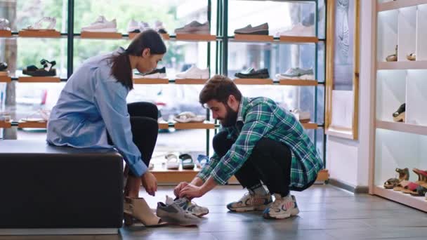 Dans la boutique de chaussures belle jeune femme avec son petit ami ont un gars jour shopping aider à porter les chaussures — Video