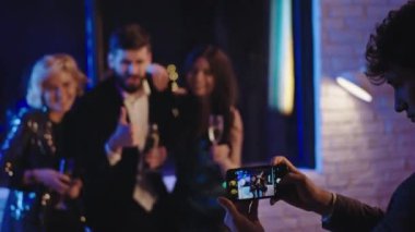 Doğum günü partisinde harika bir grup komik arkadaş hatıralar için resim çekerken diğer arkadaş da fotoğraf çekmek için telefon kullanıyor.