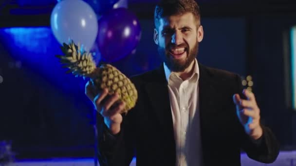 Davanti alla telecamera bel ragazzo che gioca divertente con un ananas alla festa di compleanno sorride grande. Girato su ARRI Alexa Mini — Video Stock