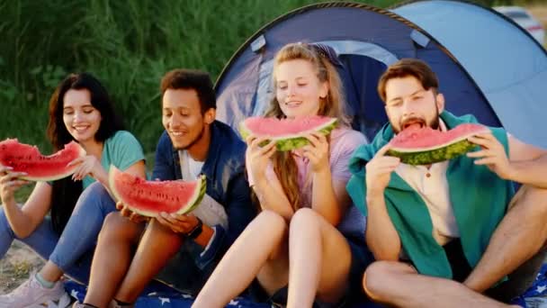 Picnic time for a group of multiracial friends eating a piece of watermelon in front of the camera smiling large. 4k — Stock Video