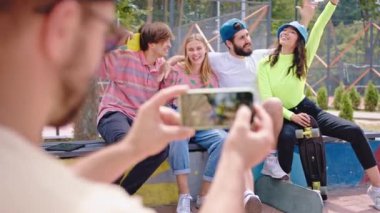 Modern bir kaykay parkında çok ırklı pozlar veren bir grup genç elinde kaykayıyla modern akıllı telefonuyla fotoğraf çekiyor. ARRI Alexa Mini 'de çekilen